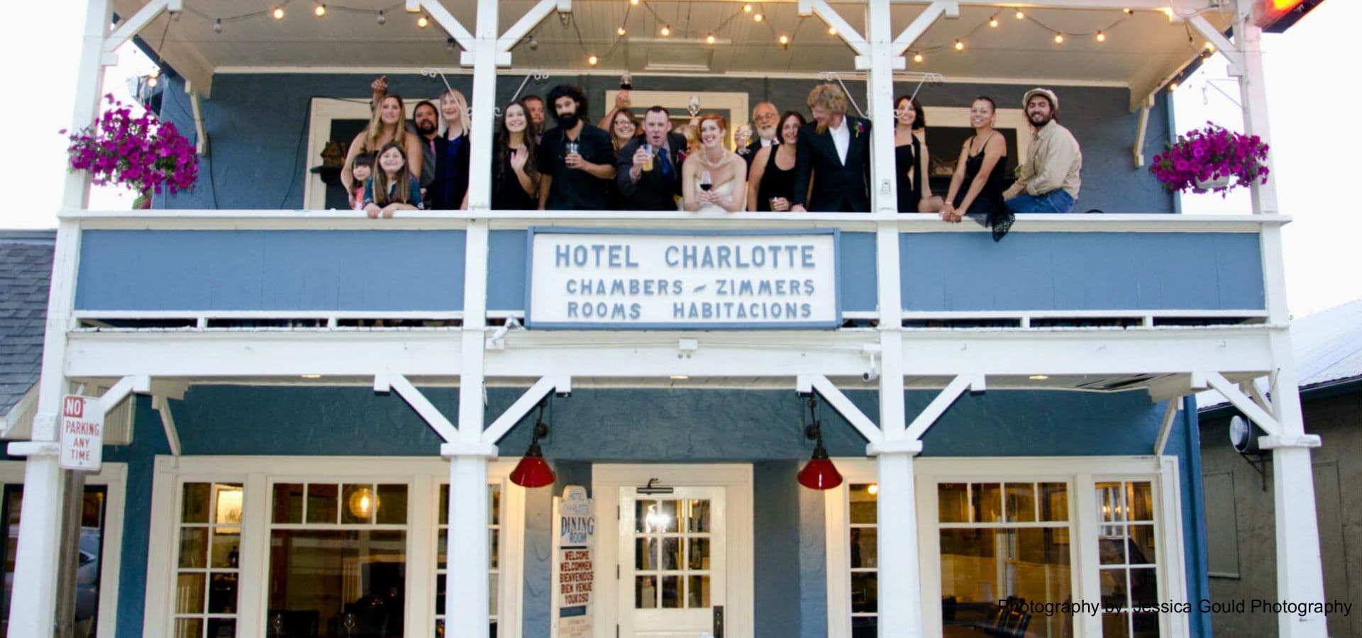 A group of people poses on the balcony of Hotel Charlotte, smiling at the camera.