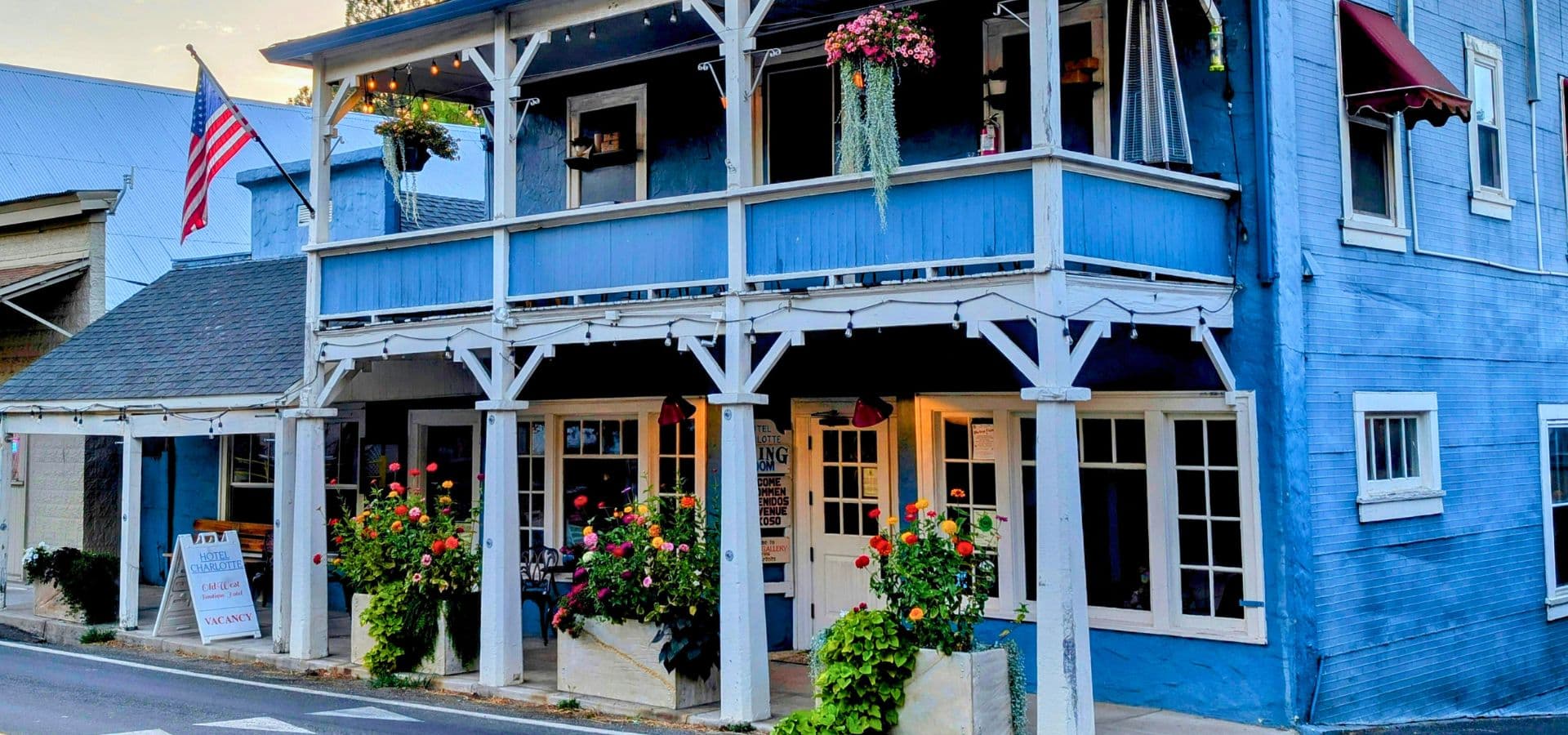 A blue, two-story building adorned with flowers and an American flag.