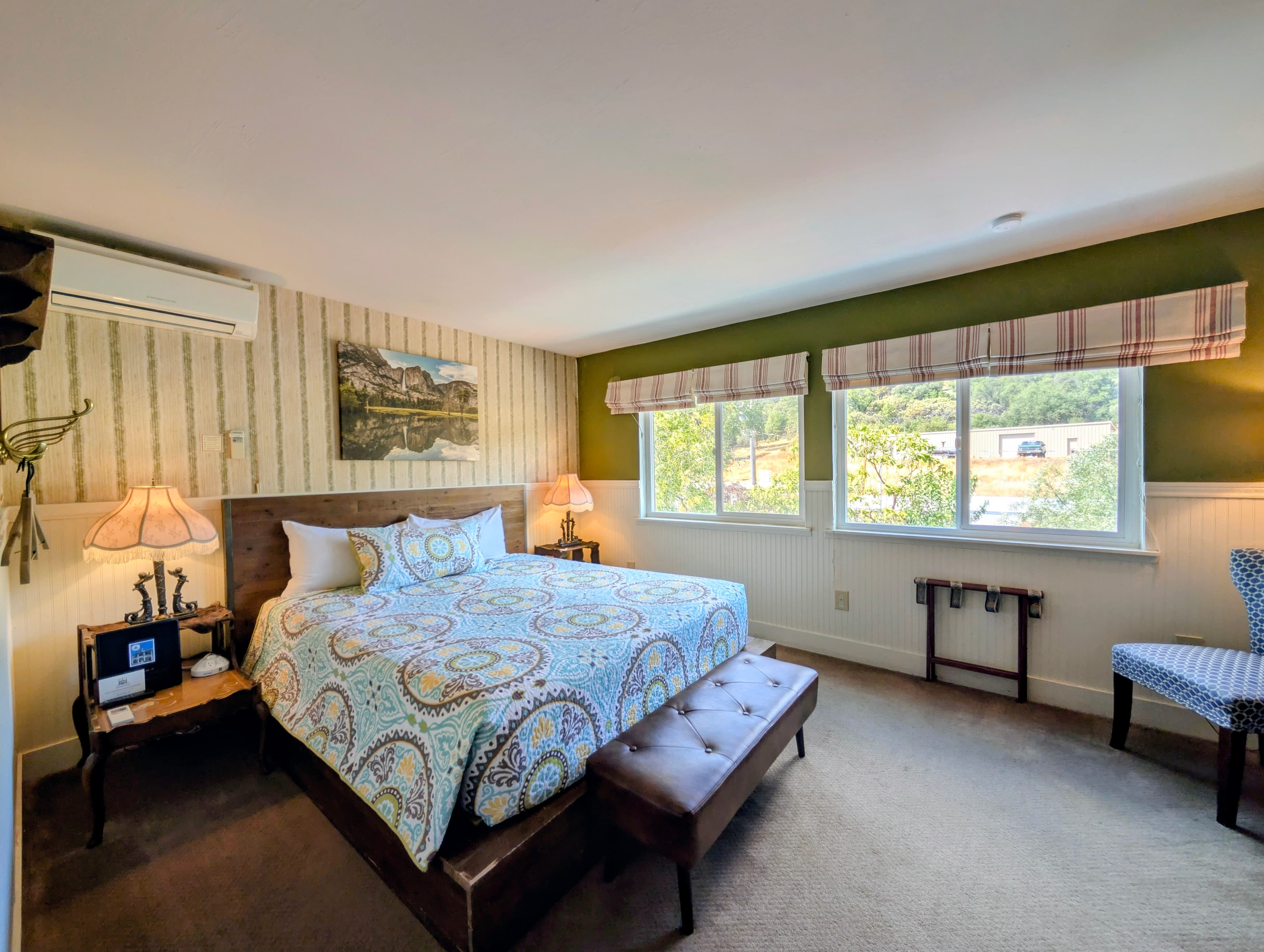 A spacious hotel room featuring a king bed with a dark wood frame, natural light from two windows, and green and striped walls.