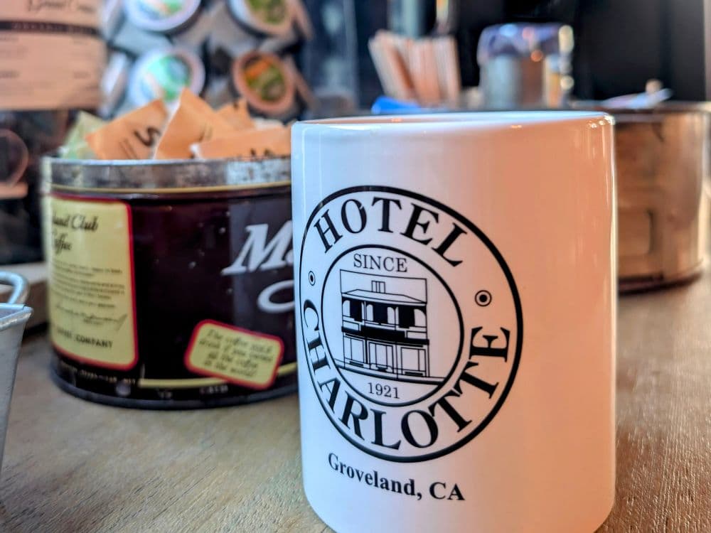A white coffee mug displays the logo of Hotel Charlotte, Groveland, CA, established in 1921.