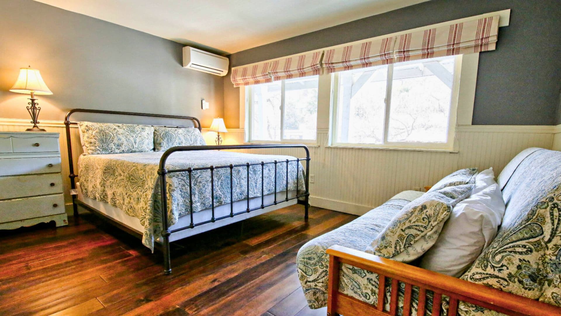 Cozy bedroom featuring a metal bed frame, decorative bedding, a futon, and large windows with natural light.