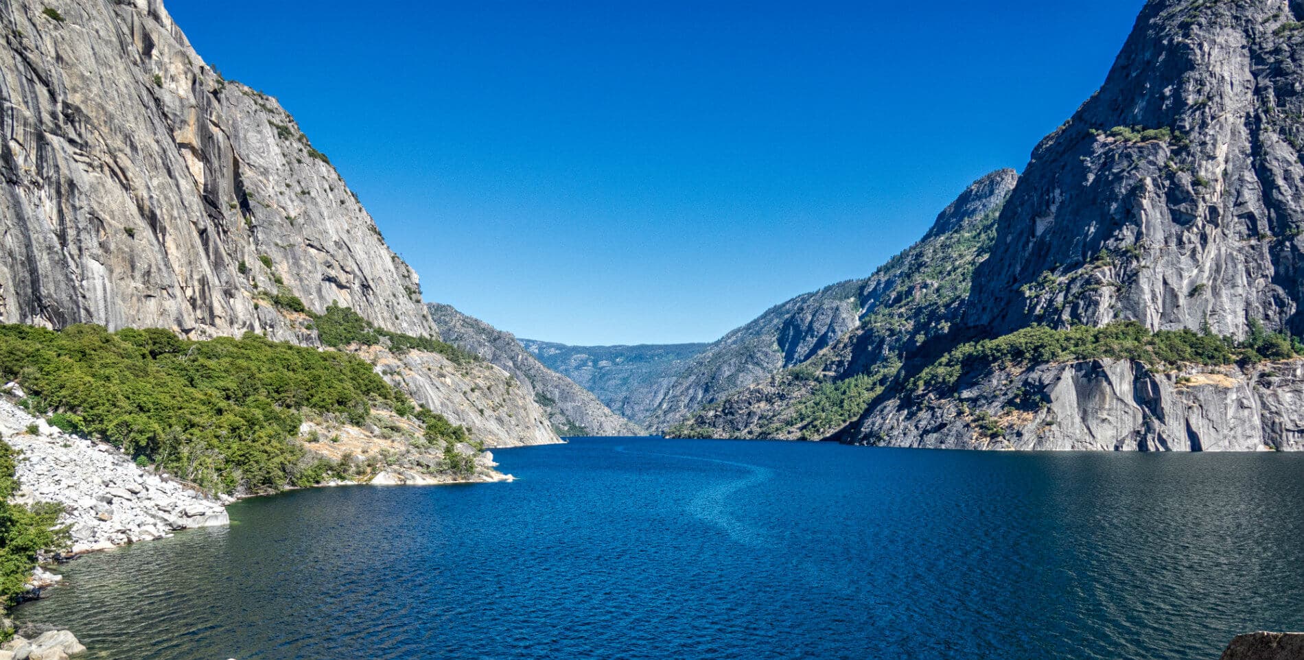 A serene lake surrounded by tall, rugged mountains under a clear blue sky.