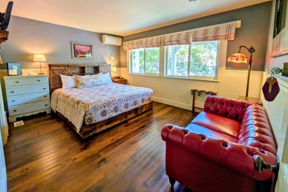 Cozy bedroom with a patterned quilt, wooden furniture, and large windows letting in natural light.