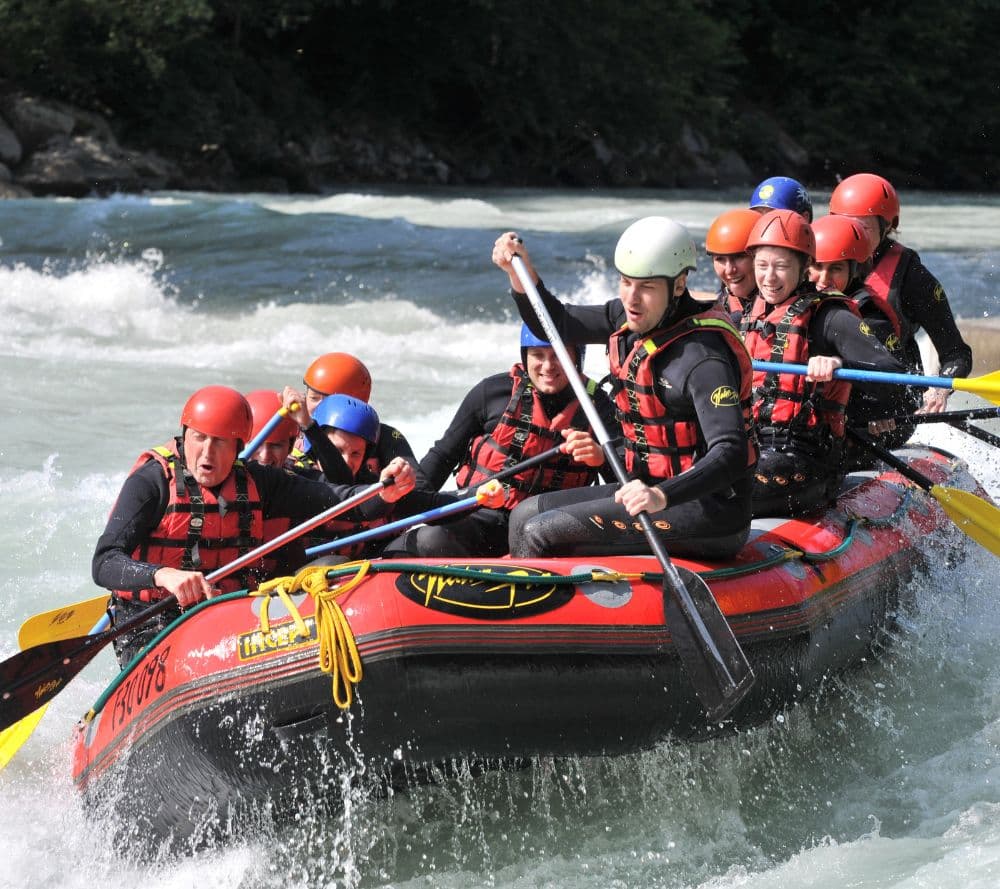 A group of people in helmets paddles a raft through turbulent waters.